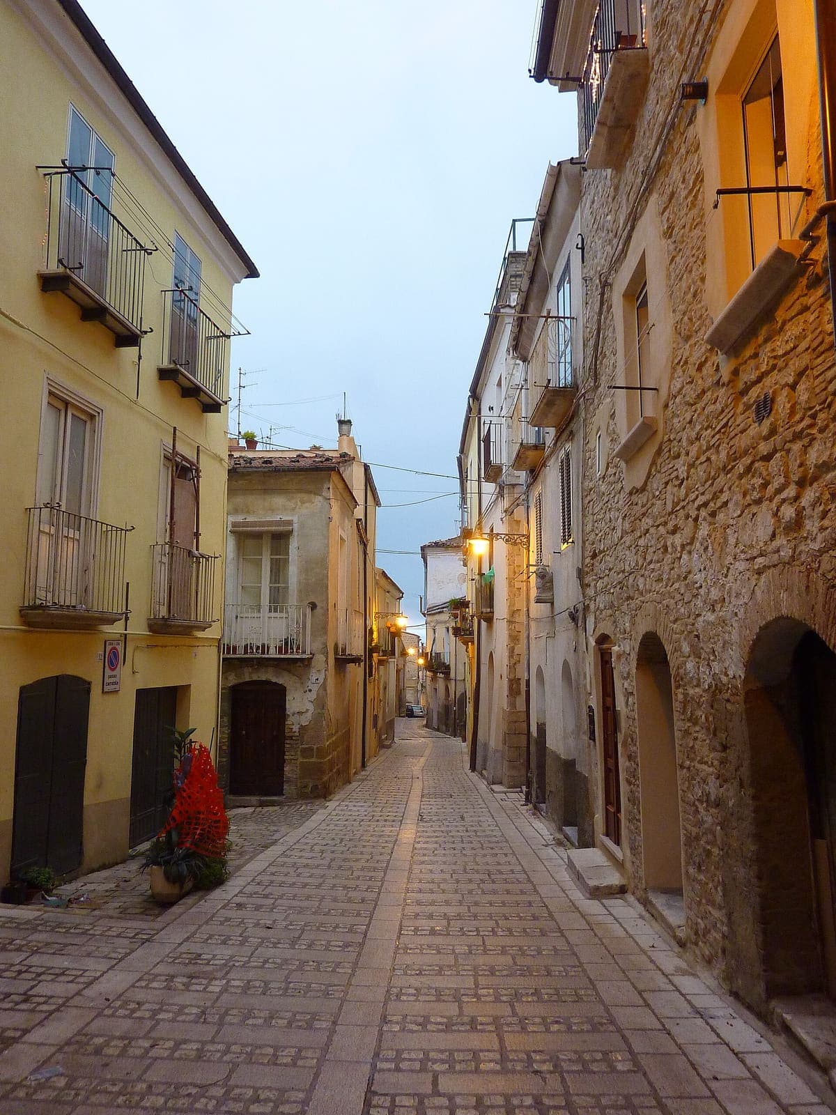 Via lastricata del centro storico di Larino al crepuscolo, tra case in pietra e lampioni accesi