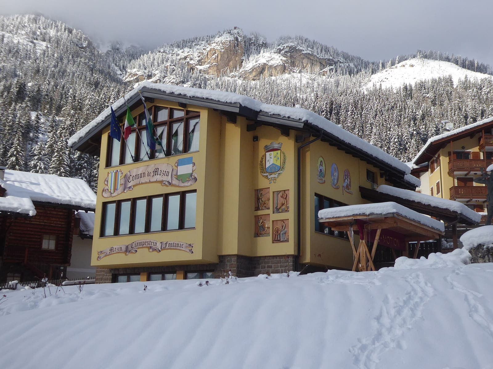 Il municipio di Mazzin a Fontanazzo sotto la neve, con le montagne della val di Fassa