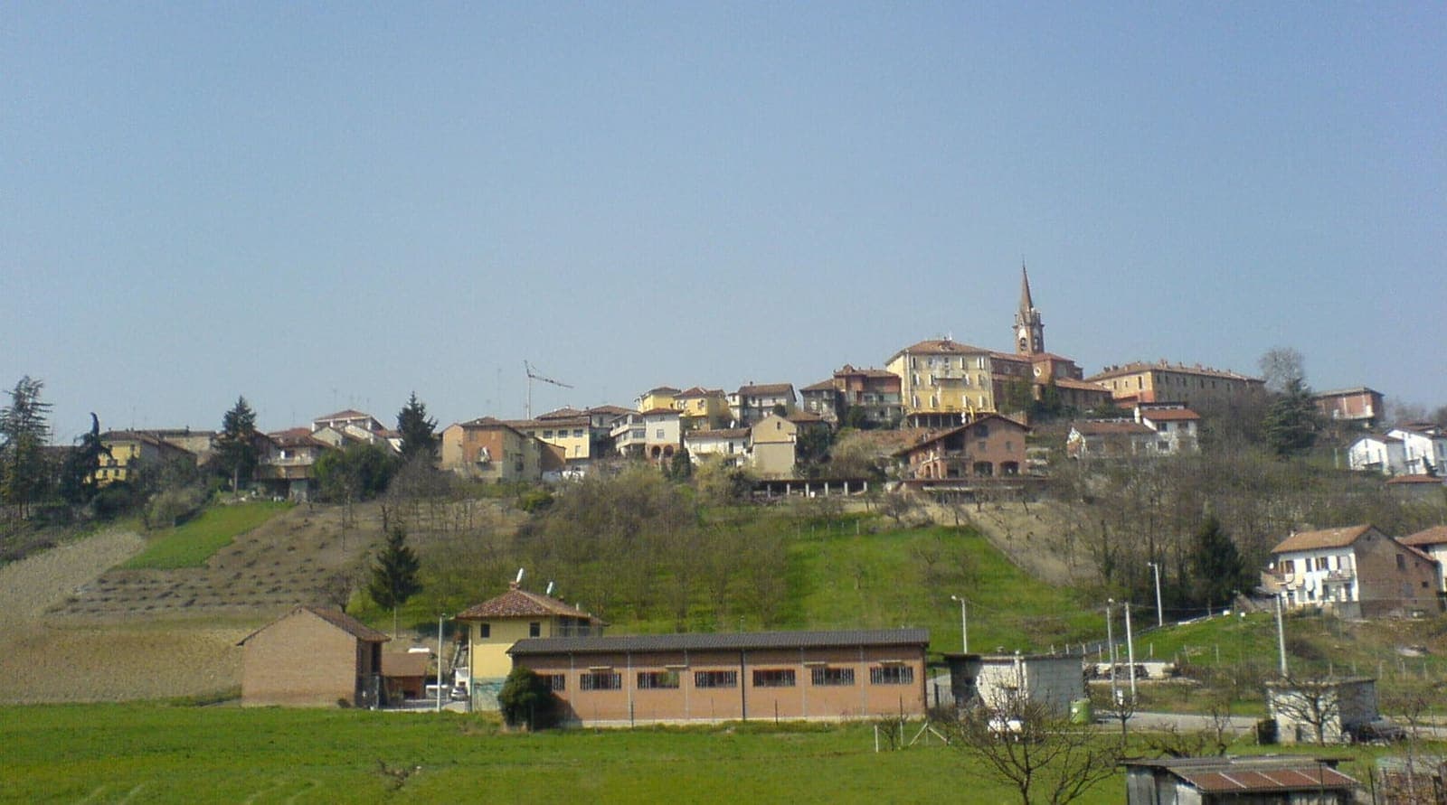 Il centro di Priocca sulla collina, con il campanile e i campi davanti