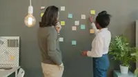 Due persone fanno brainstorming su una parete con post-it