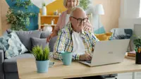 Coppia di nonni a casa davanti al laptop, lei abbraccia lui che digita